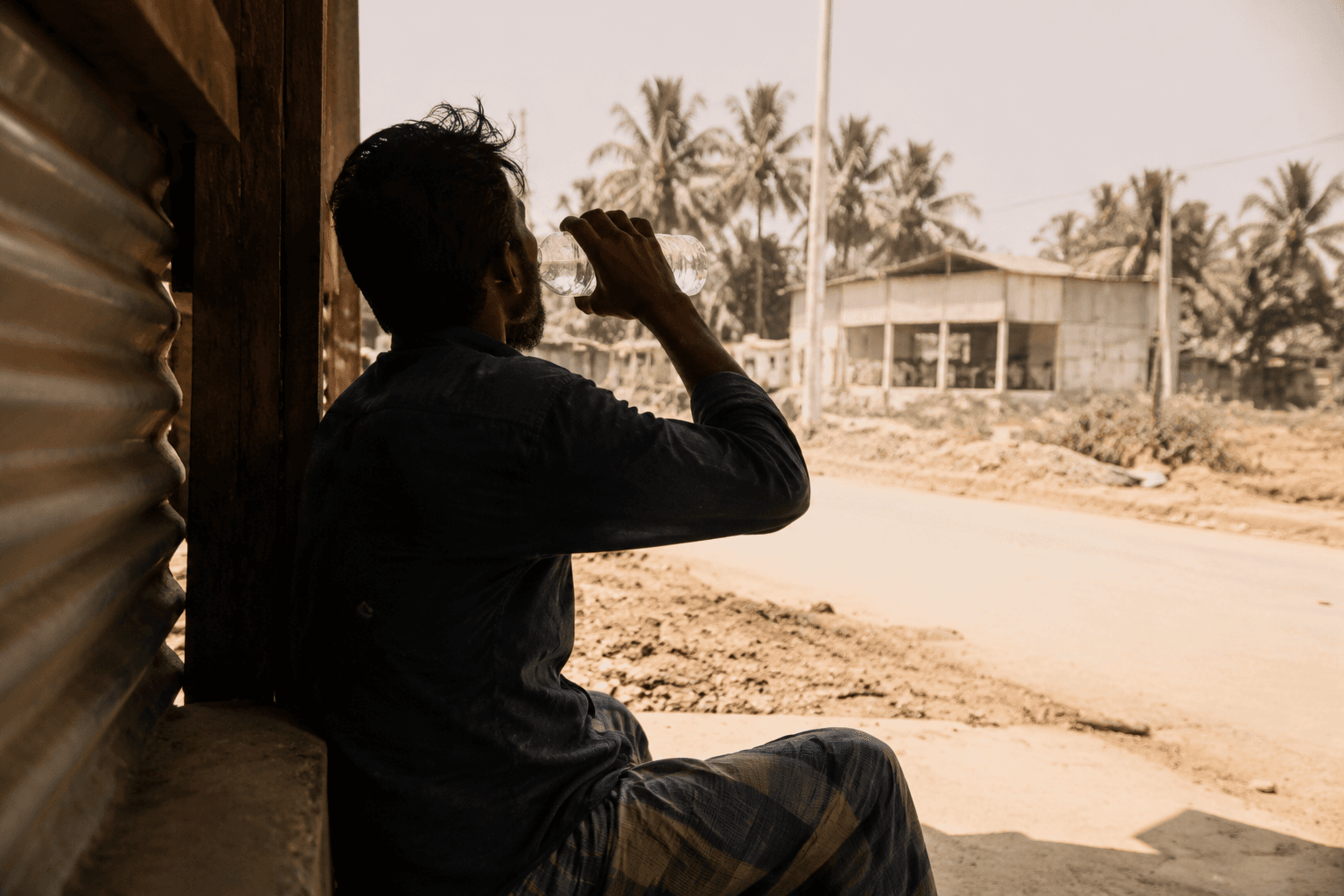 An outdoor worker rests in shade and drinks water during intense heat in Bangladesh