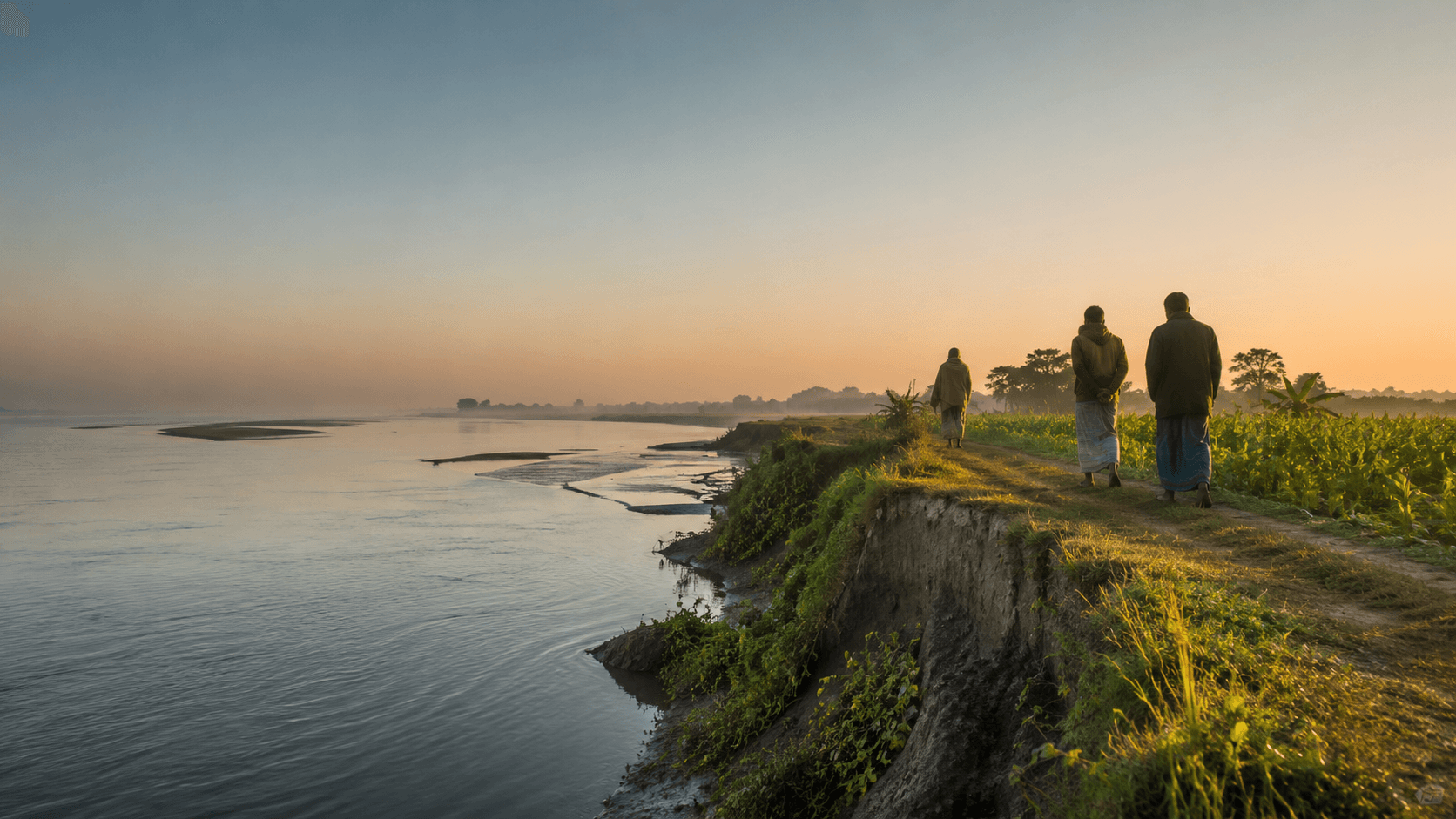 People walk beside cultivated land on an eroding riverbank in Bangladesh at dawn